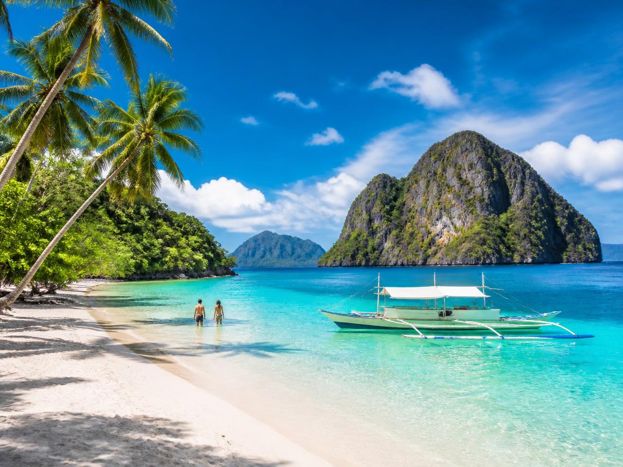 Limestone karst cliffs rising from a turquoise lagoon with a traditional outrigger bangka boat in El Nido, Palawan