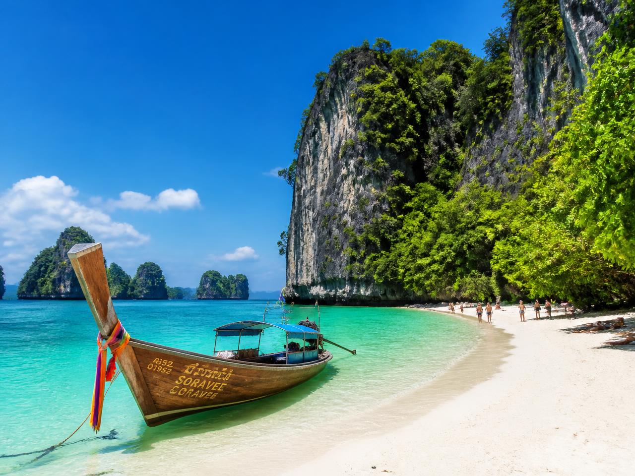 Longtail boats on emerald water beneath towering jungle limestone cliffs in the Phi Phi islands, Thailand